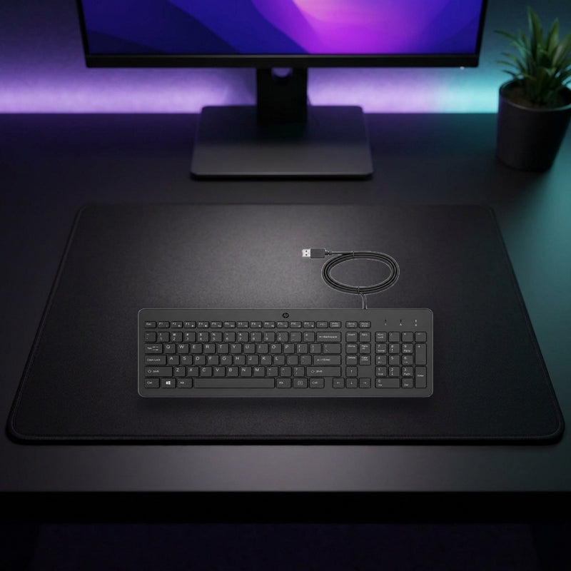 Lifestyle: HP 150 Wired Full-Size USB Keyboard – Black shown on a styled desk (actual product photo, room is illustrative)